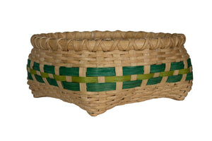 A hand-woven basket made of natural tan reed or straw, featuring a decorative horizontal band woven with dark green and light olive green strips, isolated on a white background.